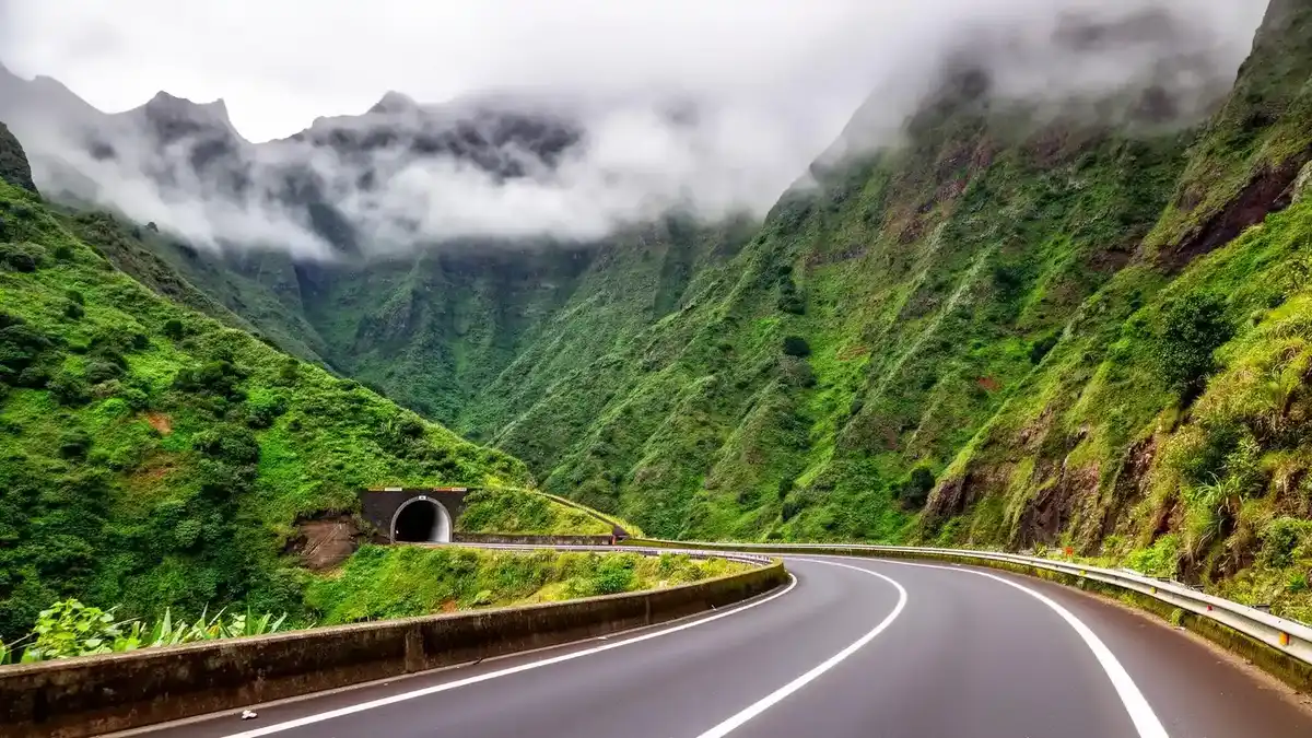 Winding mountain road through Madeira's lush green valleys with tunnel entrance visible
